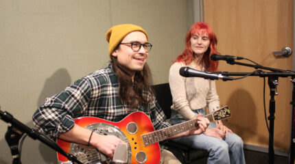 Two adults sitting behind microphones, one playing a dobro