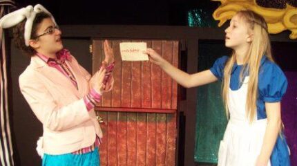 Two teens in costume acting out a scene, one with their hands up in a placating gesture, the other pointing accusingly