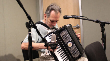 An adult playing an accordion into a microphone in a radio studio
