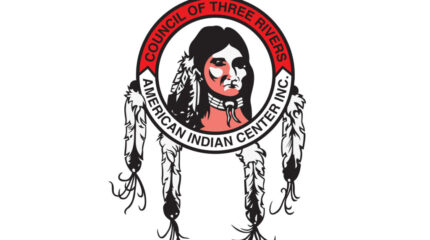 A graphic of an individual with feathers in their hair inside a circle with hanging feathers with the text "Council of Three Rivers" on the top of the circle on a red background, and "American Indian Center Inc." on the bottom of the circle on a white background