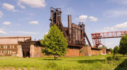 An old steel furnace in a green field with a small green tree in front