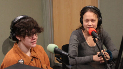 Two teens wearing headphones speaking into microphones in a radio studio