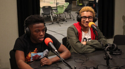 Two teens wearing headphones speaking into microphones in a radio studio