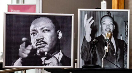 Two black and white images of an adult, one with them pointing at the camera, and the other with their hand up standing behind a microphone