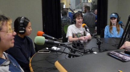 Four teens wearing headphones speaking into microphones being interviewed in a radio studio