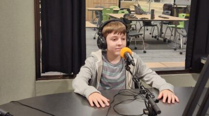 A youth wearing headphones sitting behind a microphone in a radio studio