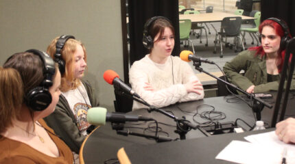 Four youth wearing headphones speaking into microphones being interviewed in a radio studio