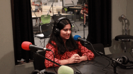 A teen wearing headphones speaking into a microphone in a radio studio