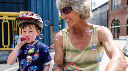 An adult looking down at a youth wearing a bike helmet and blowing bubbles