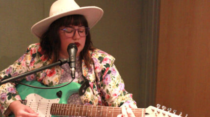 An adult playing electric guitar and singing into a microphone in a radio studio