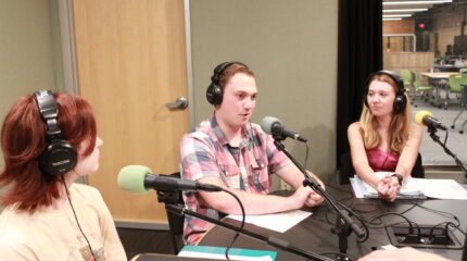 Three teens wearing headphones speaking into microphones being interviewed in a radio studio