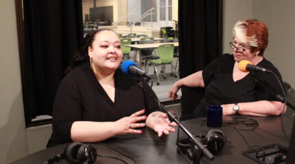 Two adults speaking into microphones in a radio studio