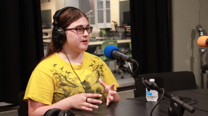 A teen wearing headphones speaking into a microphone in a radio studio