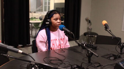 A teen wearing headphones speaking into a microphone in a radio studio