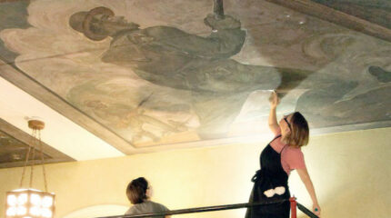 An adult painting a mural on a ceiling as another adult watches