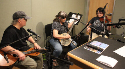 An adult playing dulcimer, an adult playing banjo, and an adult playing violin in a radio studio