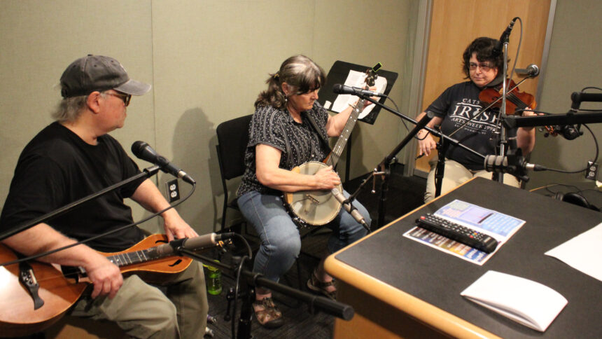 An adult playing dulcimer, an adult playing banjo, and an adult playing violin in a radio studio