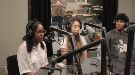 Three teens wearing headphones speaking into microphones being interviewed in a radio studio