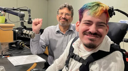 Two adults smiling at the camera in a radio studio, one holding up a fist