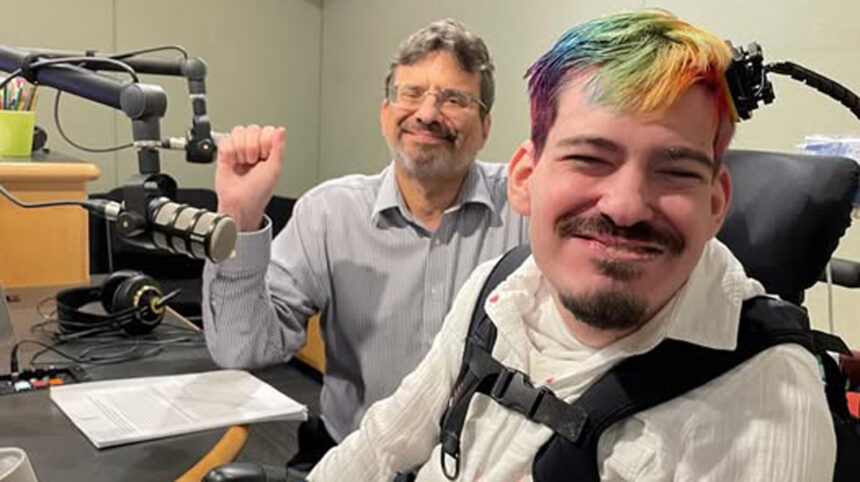 Two adults smiling at the camera in a radio studio, one holding up a fist