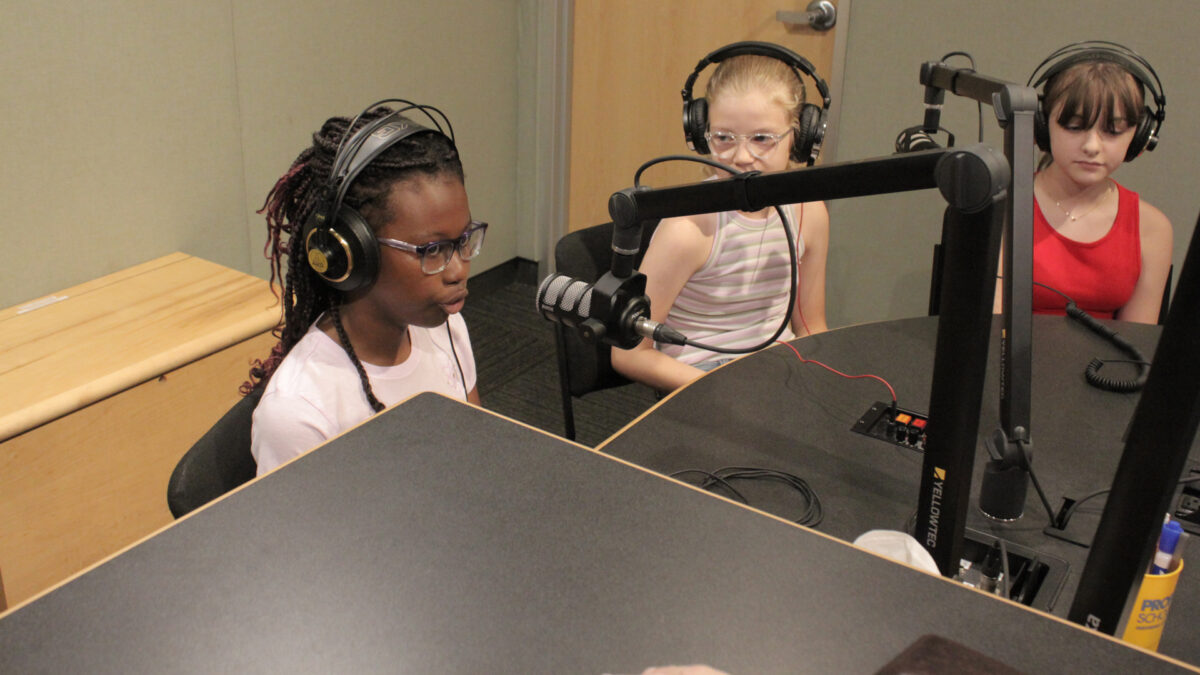 Three youth wearing headphones speaking into microphones in a radio studio