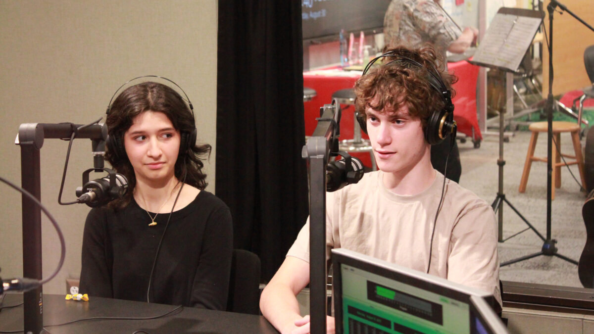 Two teens wearing headphones speaking into microphones in a radio studio