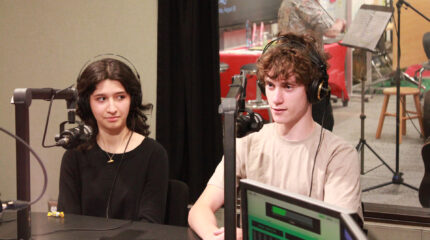 Two teens wearing headphones speaking into microphones in a radio studio