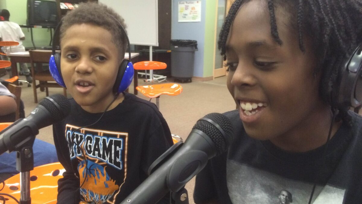 Two youth wearing headphones speaking into microphones in a library