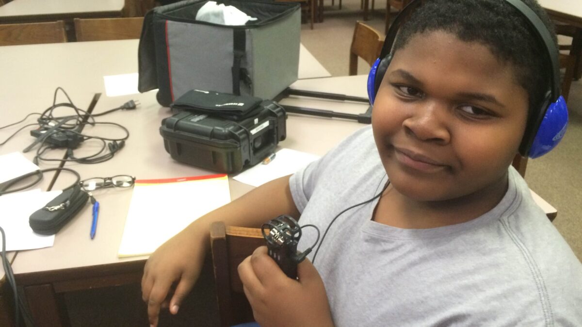 A youth wearing headphones holding a portable recorder in a library