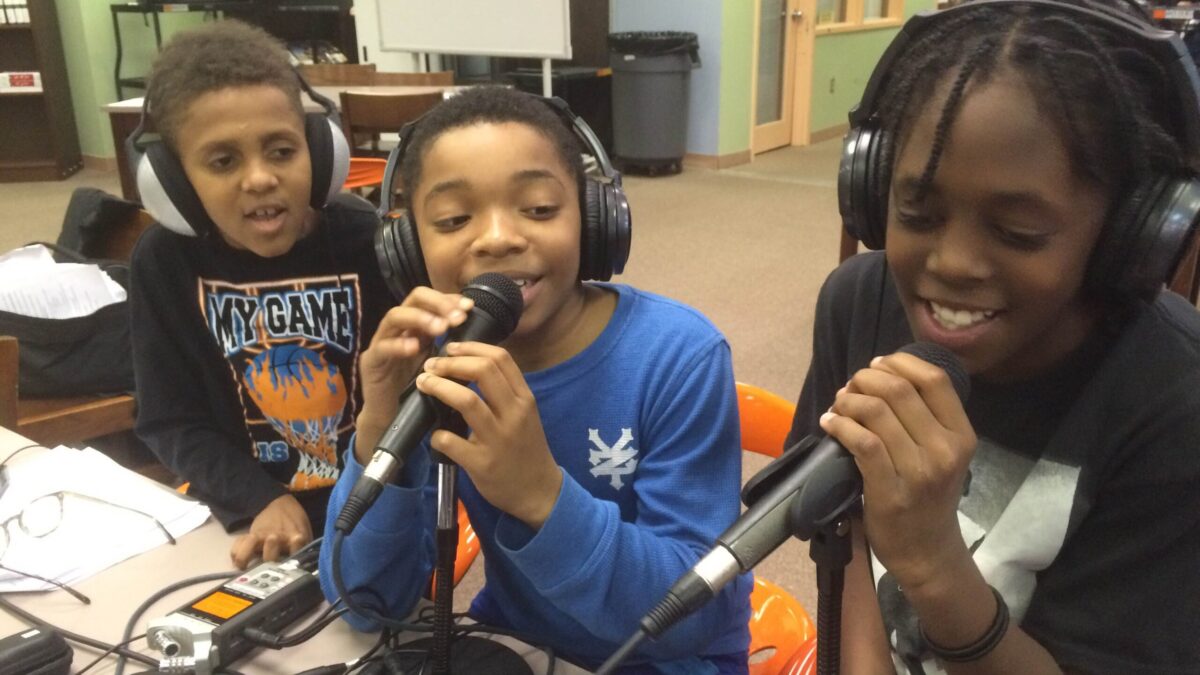 Three youth wearing headphones speaking into microphones in a library