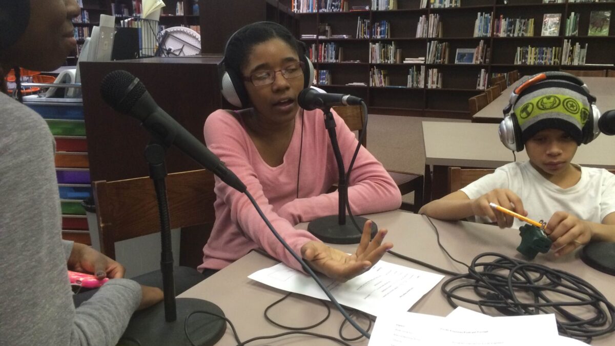 Three youth wearing headphones speaking into microphones in a library