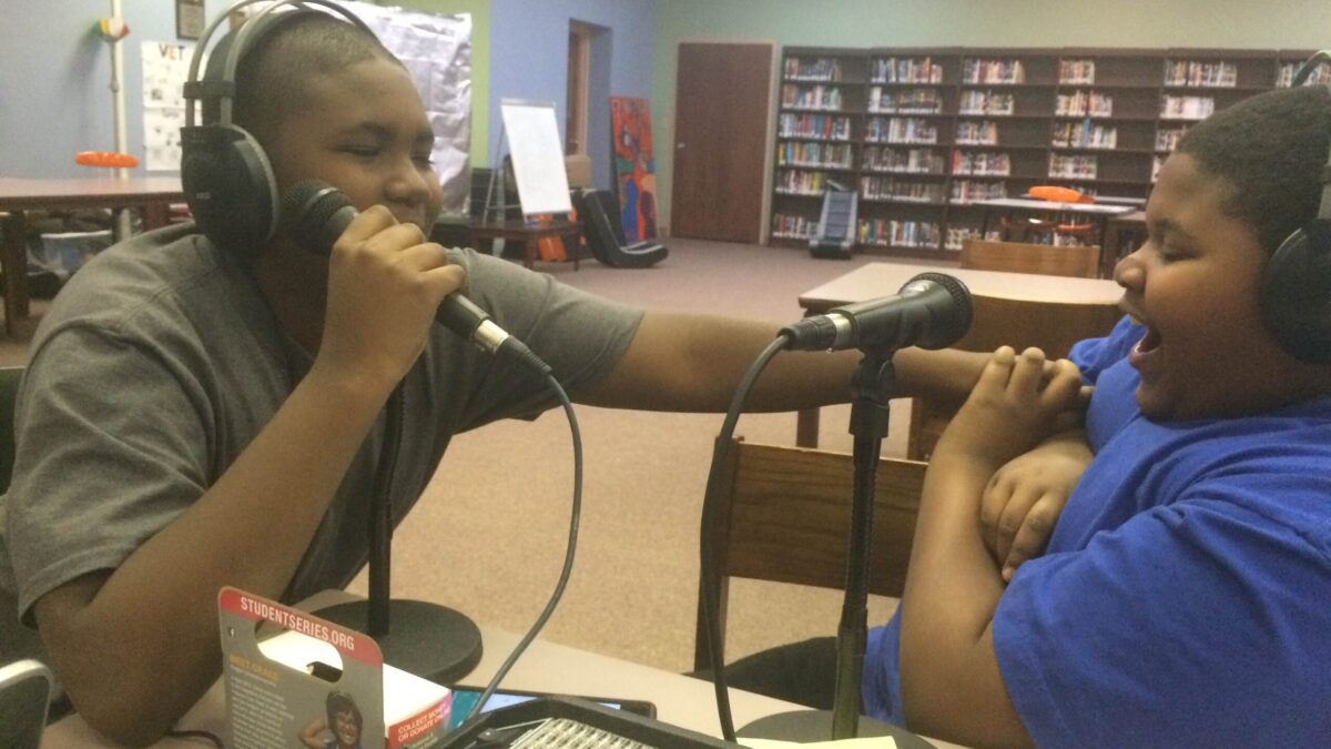 Two youth wearing headphones laughing into microphones in a library