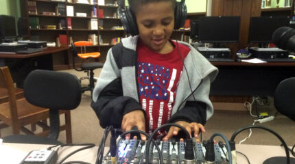 A youth wearing headphones interacting with a mixing board