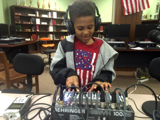 A youth wearing headphones interacting with a mixing board