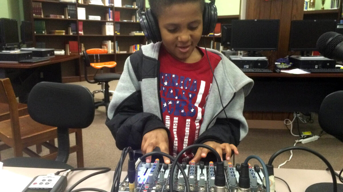 A youth wearing headphones interacting with a mixing board