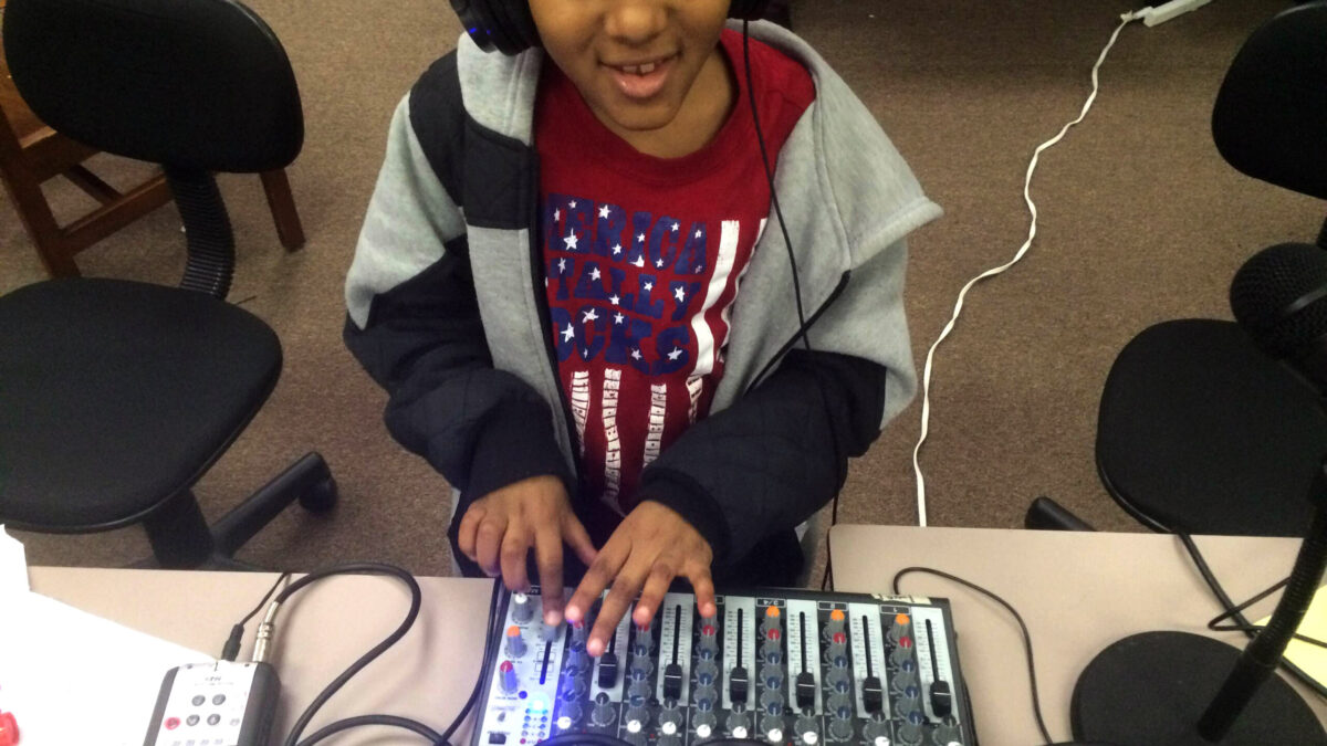 A youth wearing headphones interacting with a mixing board