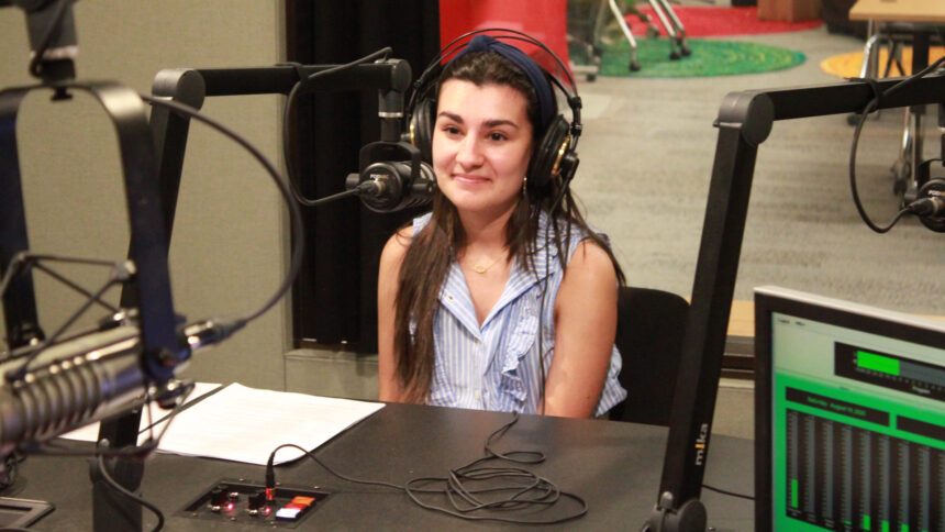 A teen wearing headphones sitting behind a microphone in a radio studio