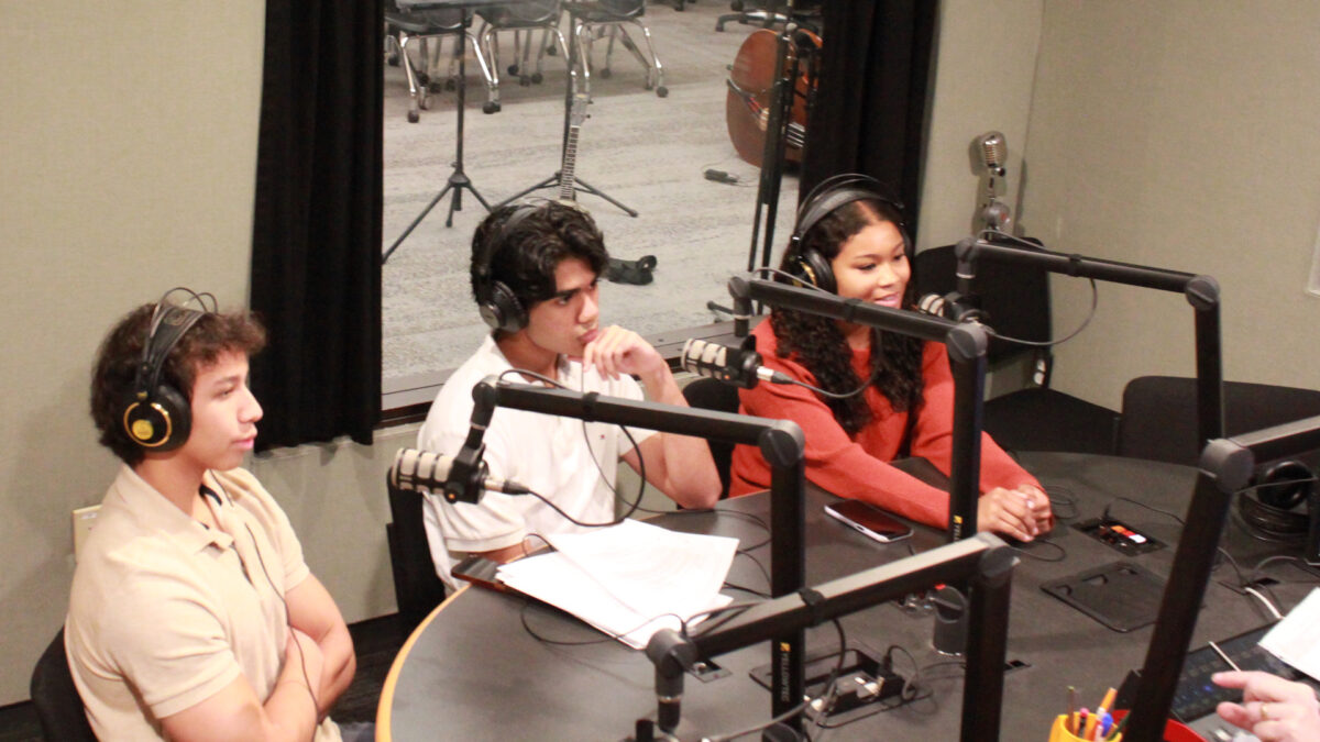 Three teens wearing headphones speaking into microphones being interviewed in a radio studio