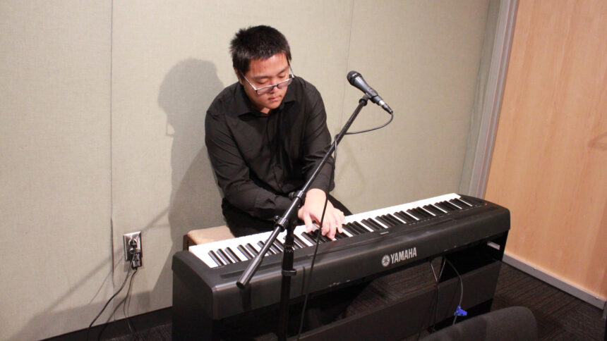 A teen playing a piano keyboard behind a microphone in a radio studio