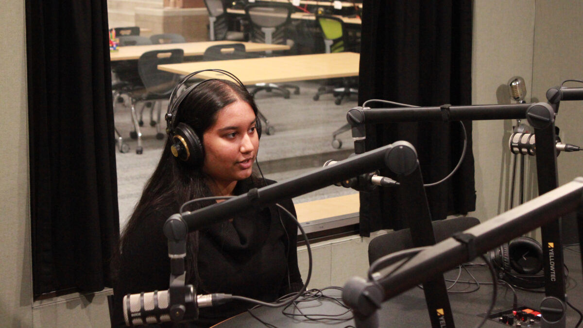 A teen wearing headphones speaking into a microphone in a radio studio