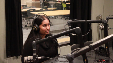 A teen wearing headphones speaking into a microphone in a radio studio