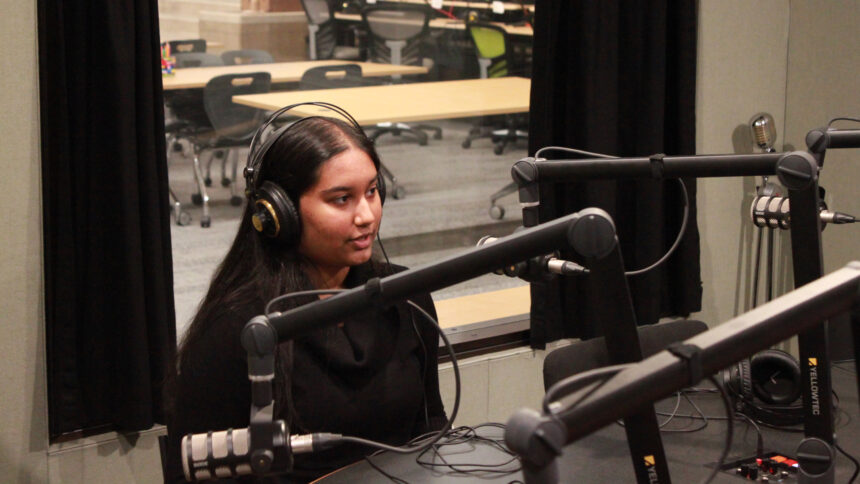 A teen wearing headphones speaking into a microphone in a radio studio