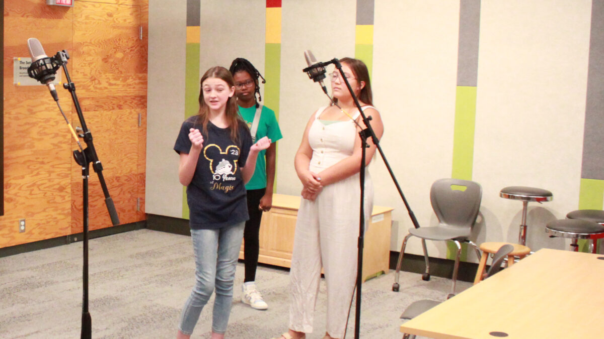 Three youth singing in a choir standing behind two microphones
