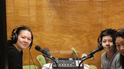 Three people in a recording booth using audio recording equipment.