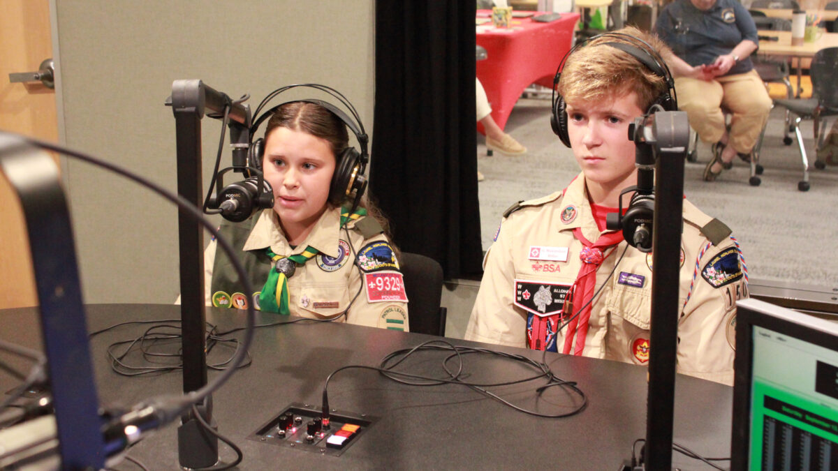 Two youth wearing headphones speaking into microphones in a radio studio