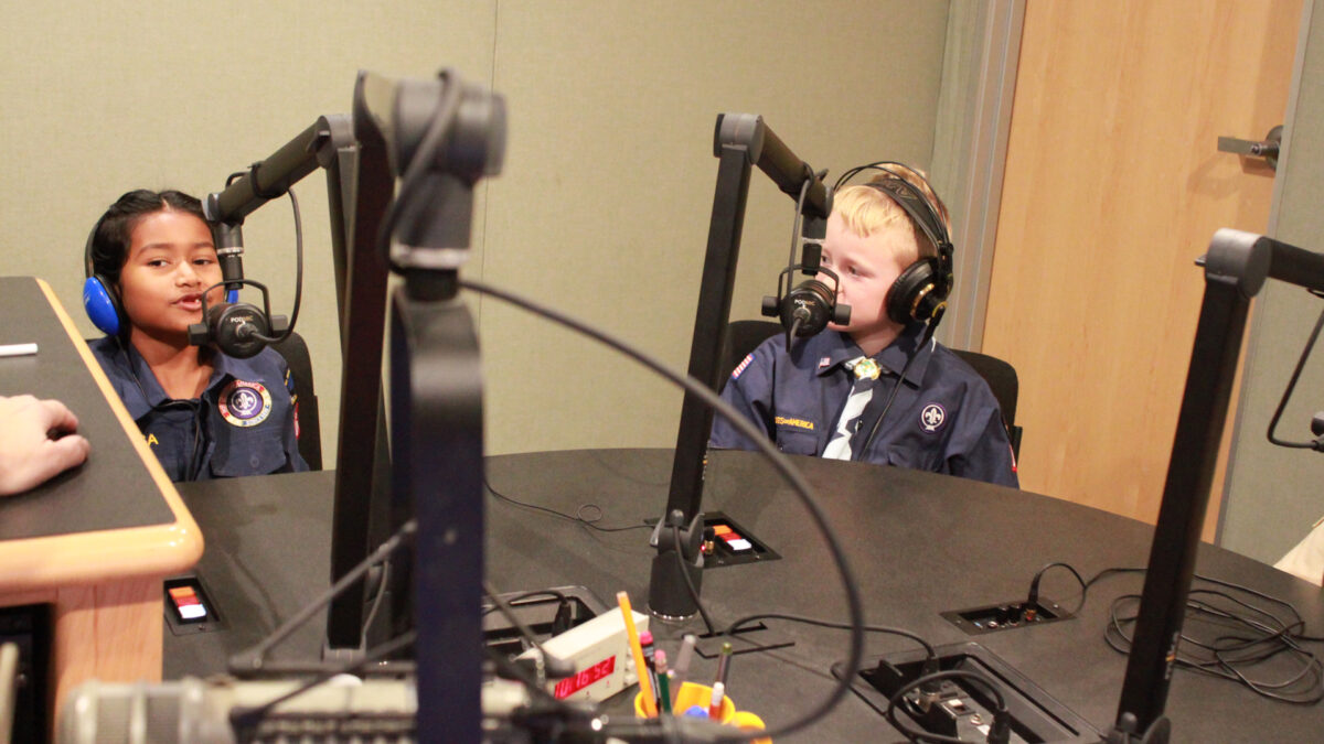 Two youth wearing headphones speaking into microphones in a radio studio