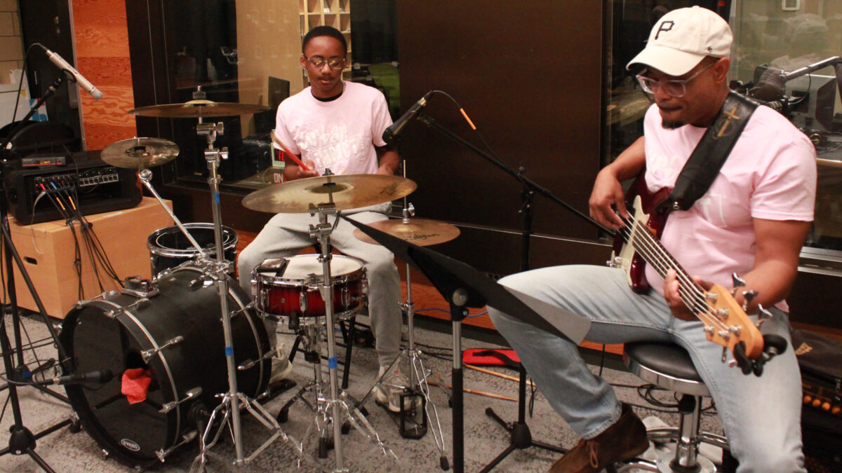 A teen playing a drum set and an adult playing an electric bass