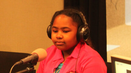 A youth wearing headphones sitting behind a microphone in a radio studio