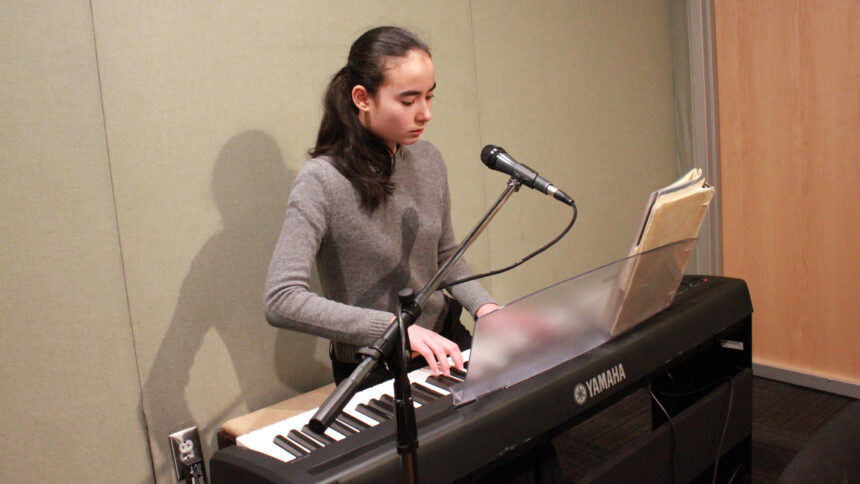 A teen playing a piano keyboard sitting behind a microphone in a radio studio