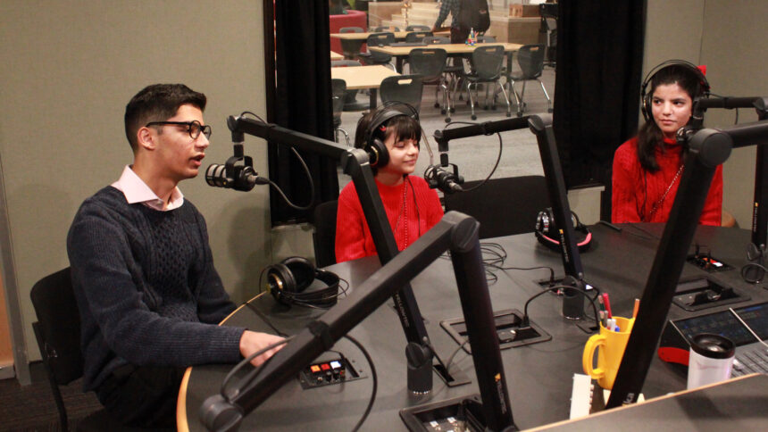 Three youth, two wearing headphones and one speaking into a microphone, in a radio studio